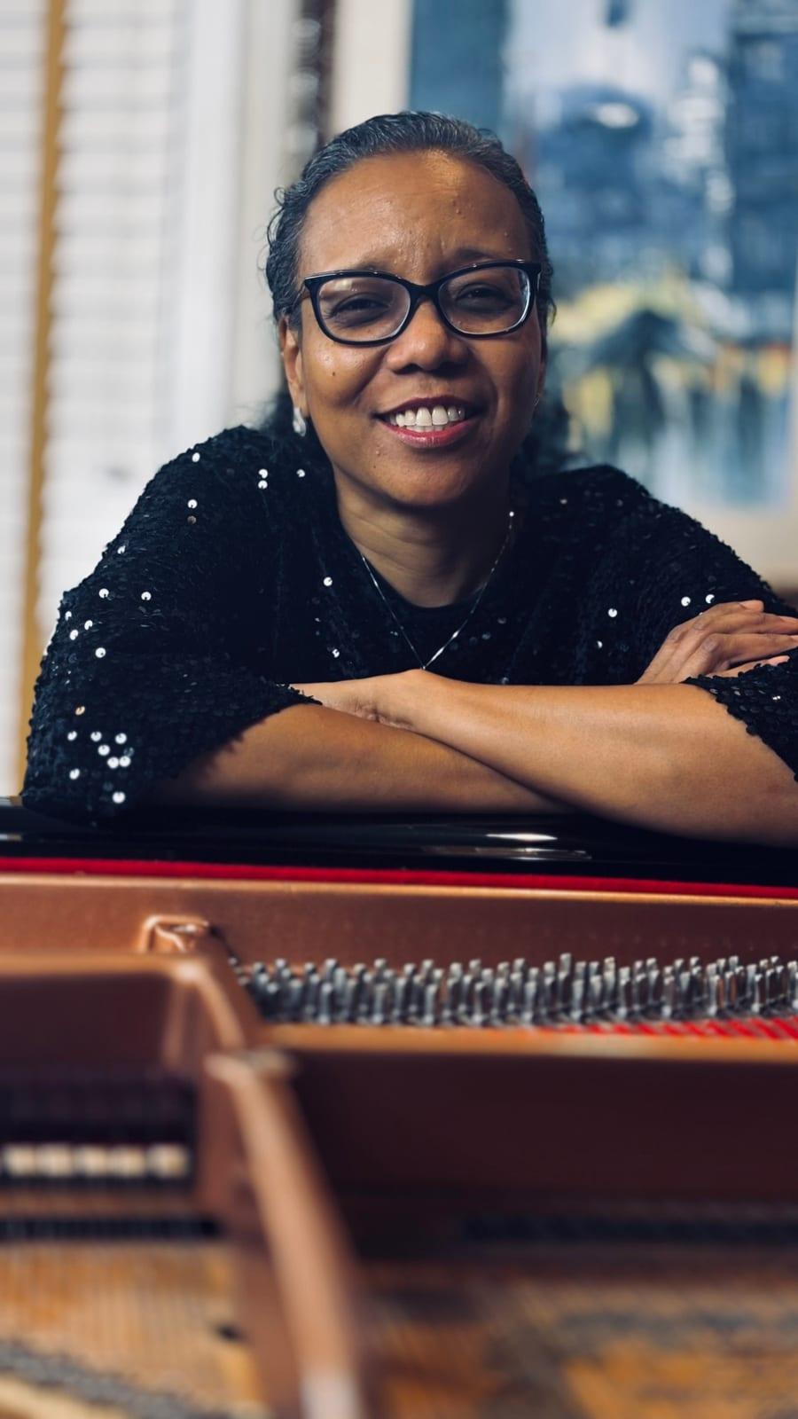 Grace J Reid leaning on a grand piano, arms folded, smiling